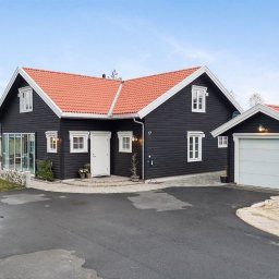 FLINK Scandinavian Houses Spółka z o.o. - Nowoczesny, ciemny dom z czerwonym dachem i białymi ramami okiennymi, z garażem i brukowanym podjazdem.