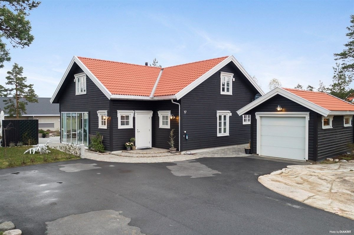 Nowoczesny, ciemny dom z czerwonym dachem i białymi ramami okiennymi, z garażem i brukowanym podjazdem.