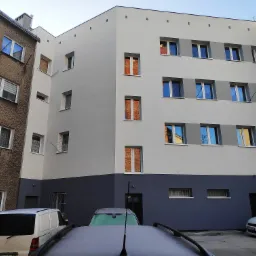 Budynek po ociepleniu i pomalowaniu elewacji w odcieniach szarości i bieli, widok z dziedzińca na odnowioną fasadę z zaparkowanymi samochodami.