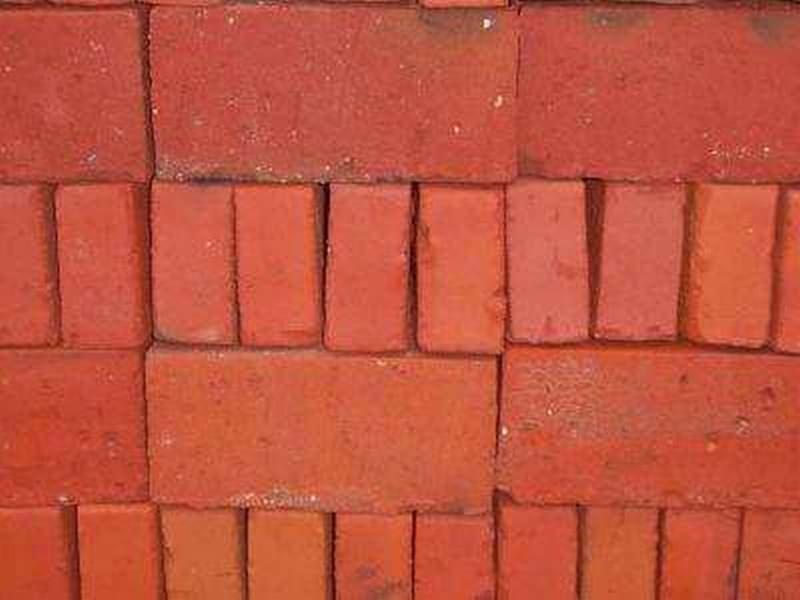 Ręcznie formowane, czerwone cegły ułożone w stos, widoczne drobne nierówności i różnice w odcieniach.