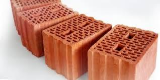 Trzy czerwone, perforowane cegły ceramiczne ułożone w rzędzie na białym tle, widoczne z perspektywy lekko z góry.