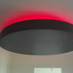 Okrągła lampa sufitowa z efektem gwiazd i czerwonym podświetleniem LED, zamontowana w pomieszczeniu z białymi ścianami.