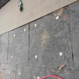 Tectum - Zieliński Łukasz - Widok z góry na czarną papę dachową mocowaną do podłoża za pomocą metalowych podkładek i gwoździ, widoczne narzędzia i fragment membrany dachowej.