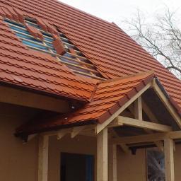 Tectum - Zieliński Łukasz - Częściowo położony dach z czerwonej dachówki ceramicznej, widoczne łaty i folia dachowa, fragment konstrukcji drewnianej werandy w stanie surowym.