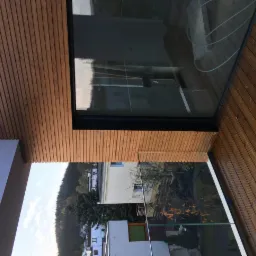 Zadaszony balkon z drewnianą podłogą i sufitem z widokiem na miasto i las, przeszklona balustrada.