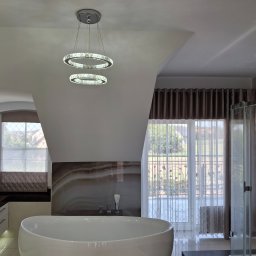 Michal88 - Nowoczesna łazienka na poddaszu z owalną wanną, marmurową ścianą i designerską lampą wiszącą. Widoczne okno z zasłonami i kabina prysznicowa.