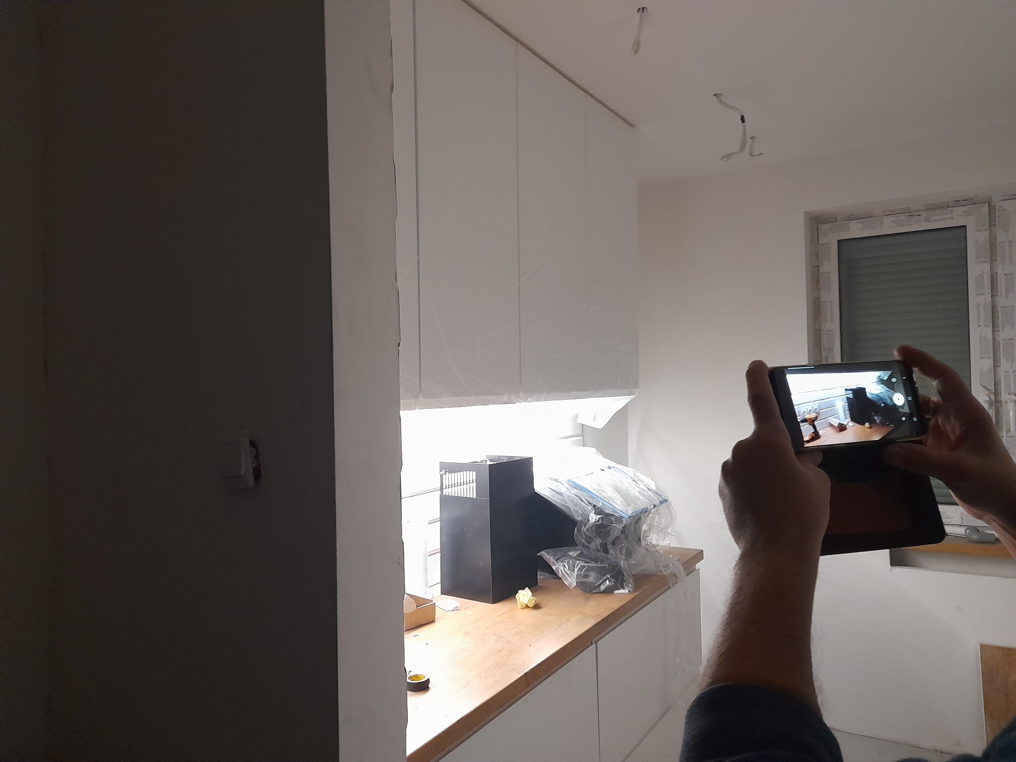 Osoba robi zdjęcie tabletem nowej, białej zabudowy kuchennej w trakcie montażu, widoczne kartony i folie ochronne na blacie.