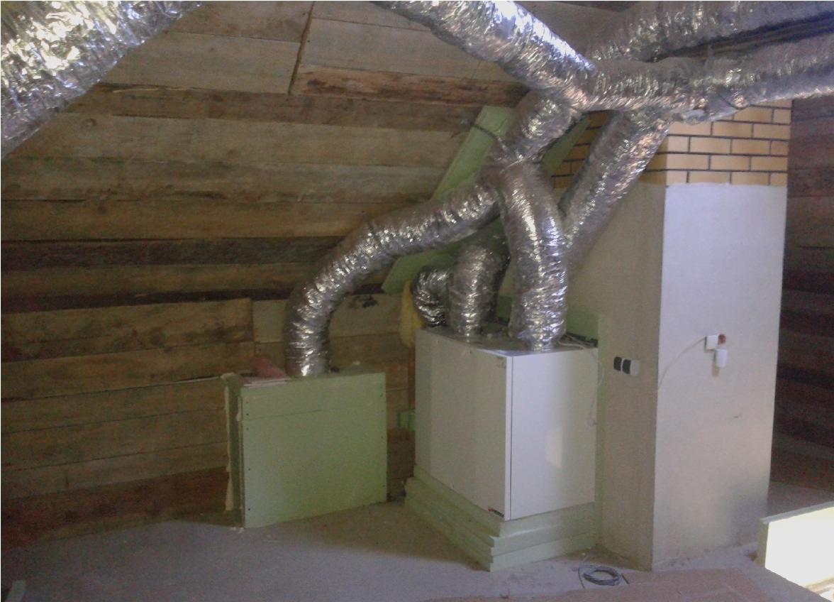 Instalacja wentylacji na poddaszu z widocznymi przewodami wentylacyjnymi i elementami montażowymi. Widoczne drewniane elementy konstrukcji dachu.