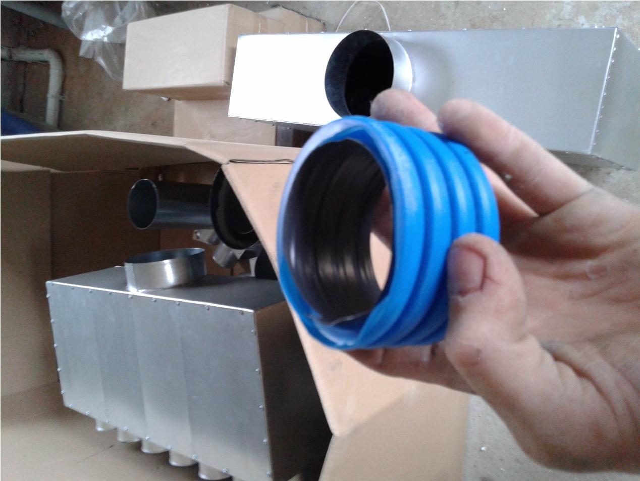 Niebieski karbowany łącznik w dłoni na tle metalowych elementów wentylacyjnych w kartonach. Detal instalacji wentylacyjnej w trakcie montażu.