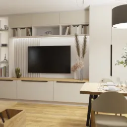 Jasne wnętrze salonu z jadalnią, minimalistyczny design, drewniany stół z nakryciem, telewizor na ścianie z dekoracyjną zabudową, stolik kawowy z laptopem i filiżanką.