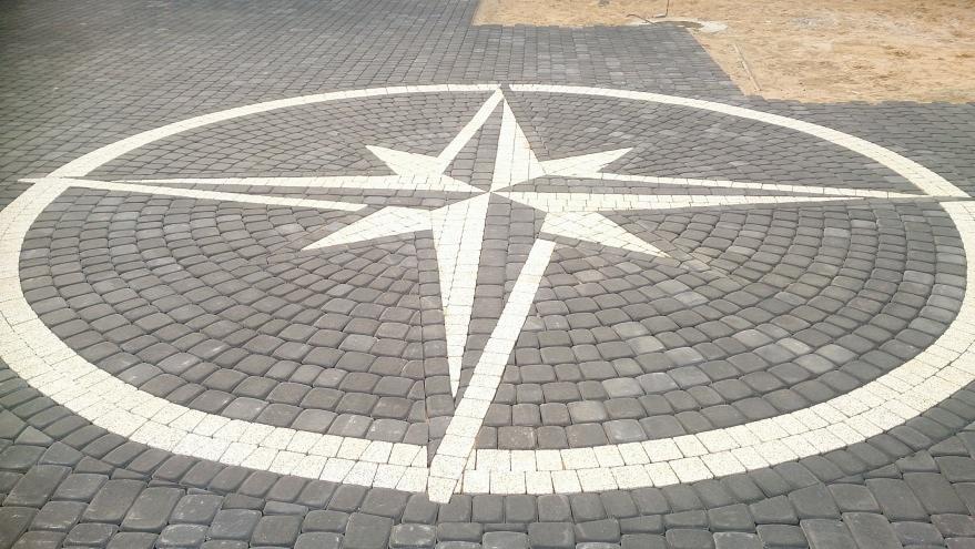 Szara kostka brukowa ułożona w okrągły wzór z białym kompasem pośrodku, widok z góry.