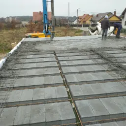 Wylewanie betonu na strop Teriva z widocznym zbrojeniem, pompy do betonu i betoniarki w tle, budowa domu jednorodzinnego w trakcie realizacji.