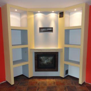 Wnęka kominkowa z półkami po bokach, oświetlenie punktowe nad kominkiem, ściany pomalowane na kremowo, boczne ściany czerwone, brązowa podłoga z płytek.