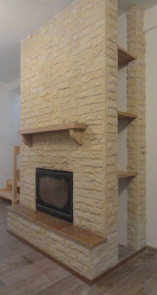 Obudowa kominka z kamienia dekoracyjnego z drewnianą półką i wnęką z półkami, widoczna część schodów.