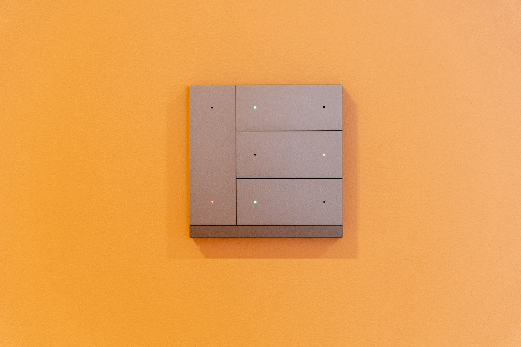 Szary panel sterowania inteligentnego domu z delikatnymi diodami LED na pomarańczowej ścianie.