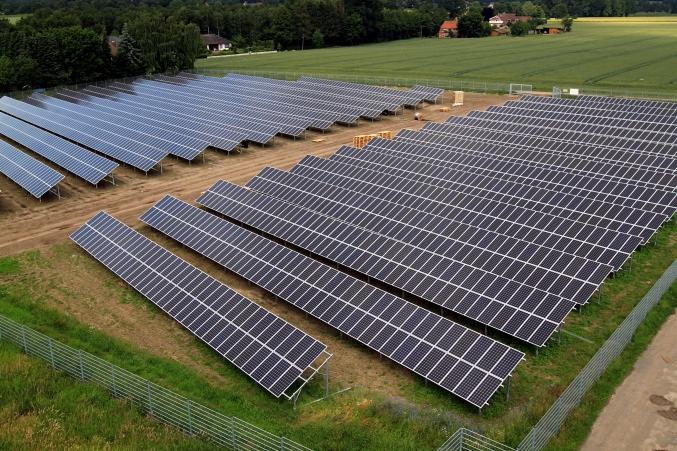 Rozległa farma paneli słonecznych na polu, widok z góry, ogrodzenie z metalowej siatki wzdłuż obrzeży.