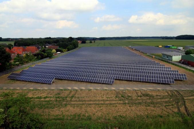 Rozległa farma paneli słonecznych na polu, widok z góry, w tle zabudowania mieszkalne i obiekty gospodarcze.