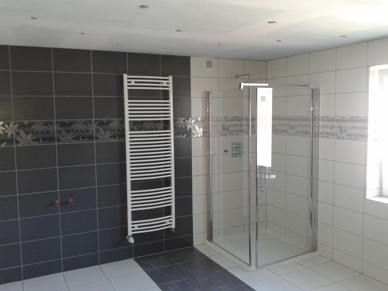 Wykończona łazienka z szarymi i białymi płytkami, dekoracyjnym pasem z motywem liści, grzejnikiem drabinkowym i szklaną kabiną prysznicową.