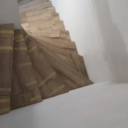 Montaż płytek imitujących drewno na krętych schodach, zabezpieczonych taśmą malarską i krzyżykami dystansowymi, widok z góry.