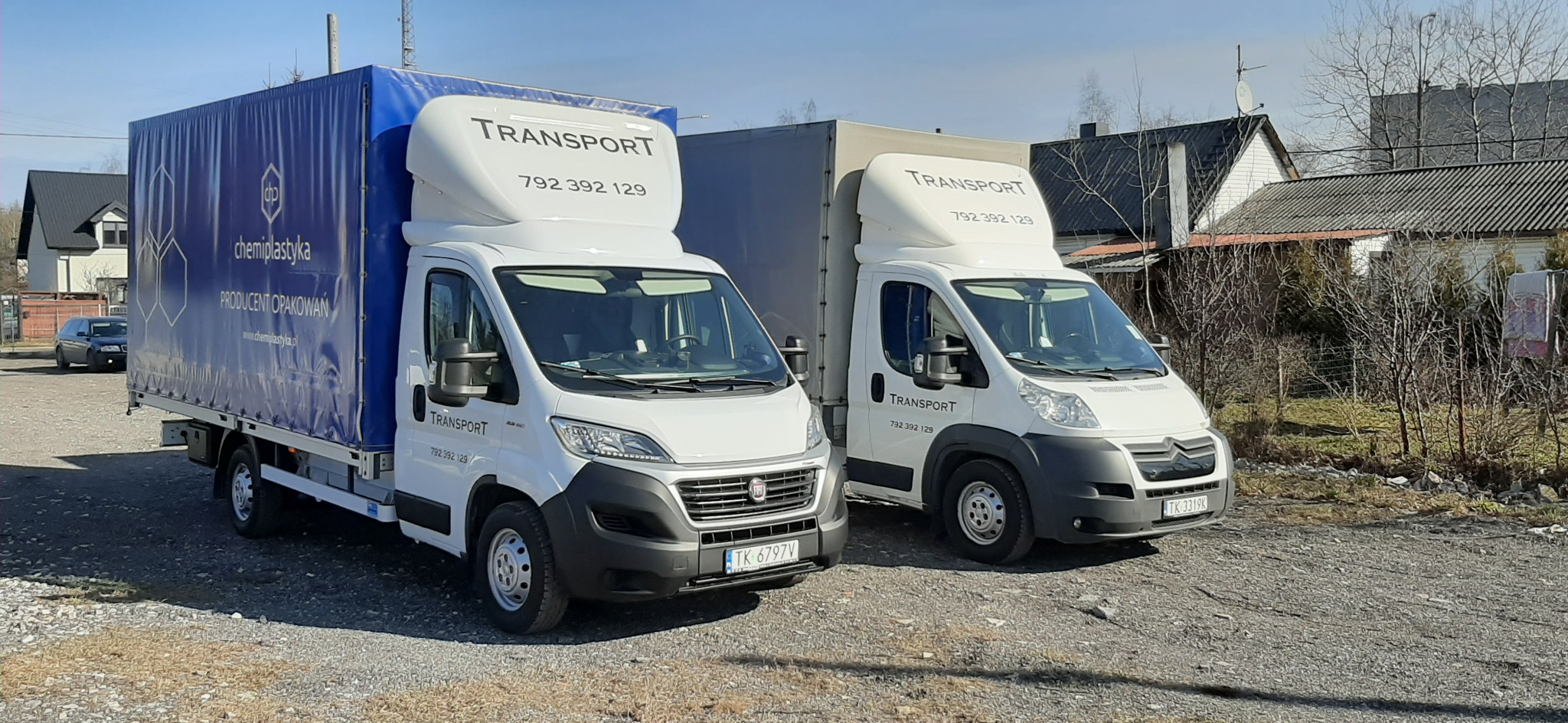 Dwa białe busy transportowe z nadrukowanym numerem telefonu i logo firmy, jeden z niebieską plandeką z logo producenta opakowań, stojące na żwirowym parkingu.