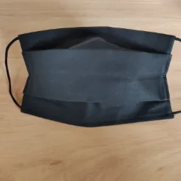 Czarna, materiałowa maska ochronna na jasnym, drewnianym stole, widoczne gumki i szwy.