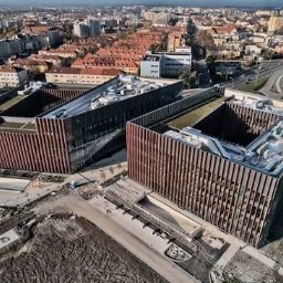 ALFA TAR Robert Tarnowski - Dwa nowoczesne budynki biurowe z elewacją w odcieniach brązu, widziane z lotu ptaka na tle miejskiego krajobrazu. Widoczne elementy konstrukcyjne i teren wokół budynków.