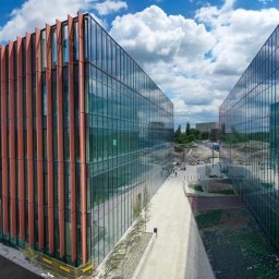 ALFA TAR Robert Tarnowski - Dwa nowoczesne biurowce z fasadą z czerwonych paneli i szklanymi ścianami, połączone chodnikiem, na tle błękitnego nieba z chmurami.