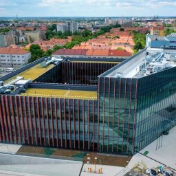 ALFA TAR Robert Tarnowski - Nowoczesny budynek biurowy z zielonym dachem i szklaną fasadą, widok z góry na tle miejskiego krajobrazu. Widoczne miejsca parkingowe dla niepełnosprawnych.