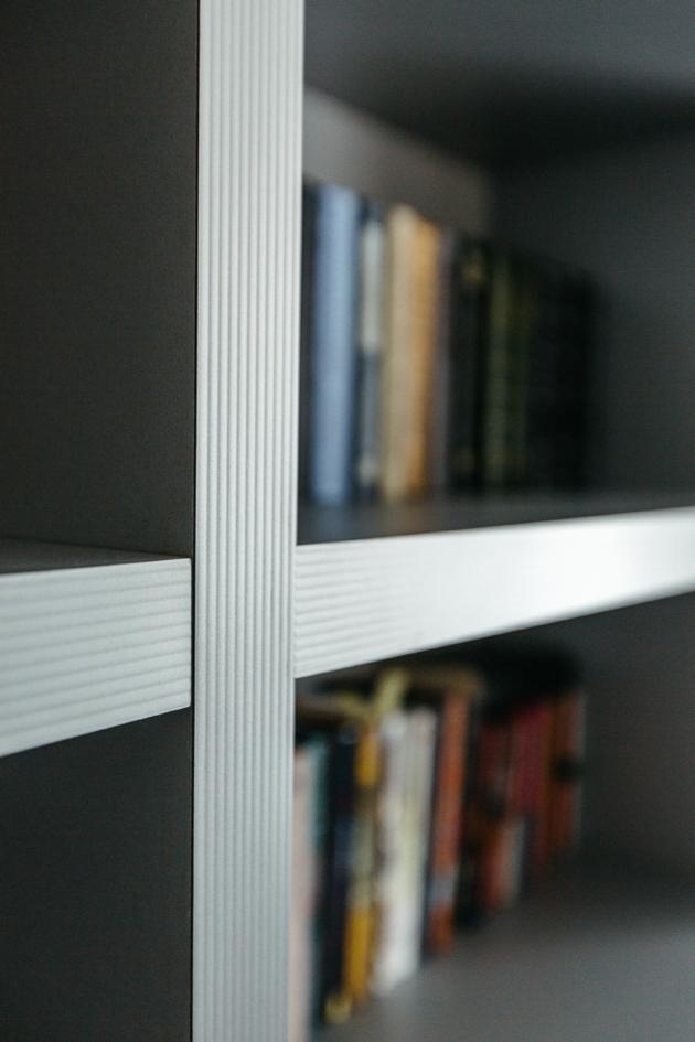 Fragment szafy wnękowej z półkami wypełnionymi książkami, widoczne pionowe i poziome elementy wykończeniowe z charakterystycznym ryflowaniem.