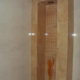 Beżowa kabina prysznicowa z mozaiką i dekoracją z trawy pampasowej, jasne płytki na ścianie. Widoczne detale wykończenia i oświetlenie.