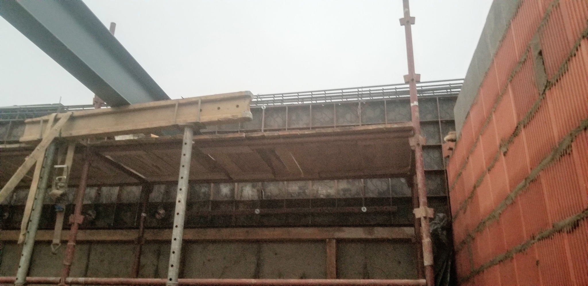 Konstrukcja szalunku pod wieniec żelbetowy z widocznym zbrojeniem i fragmentem murowanej ściany z czerwonej cegły dziurawki.