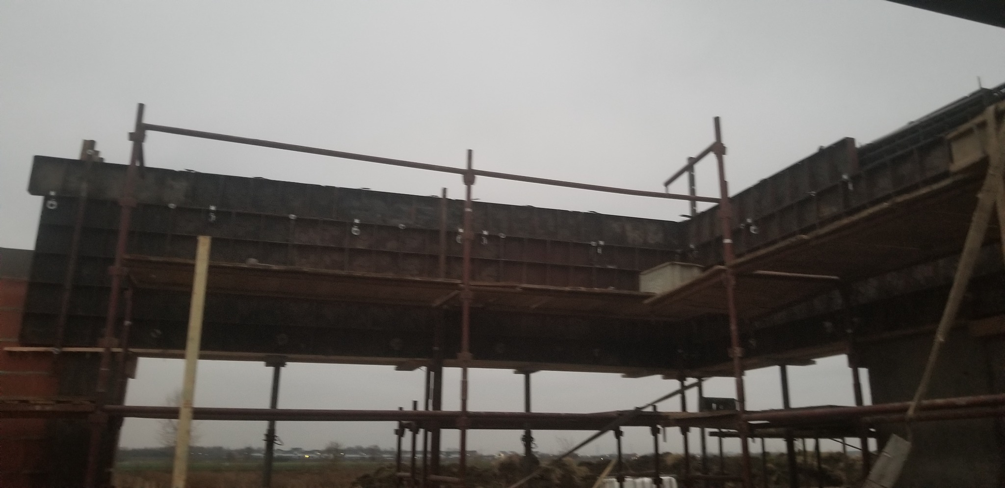 Szare szalunki na rusztowaniu podczas budowy konstrukcji żelbetowej, widok na zewnątrz przy pochmurnej pogodzie.