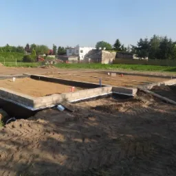 Wylane fundamenty pod dom jednorodzinny z widocznymi bloczkami betonowymi, izolacją poziomą i zasypanym piaskiem wewnątrz, widok z poziomu gruntu na placu budowy.