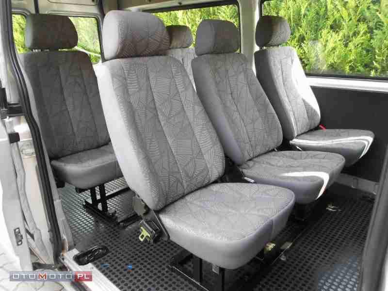 Wnętrze busa z czterema rzędami szarych foteli z geometrycznym wzorem, widoczne mocowania foteli do podłogi.