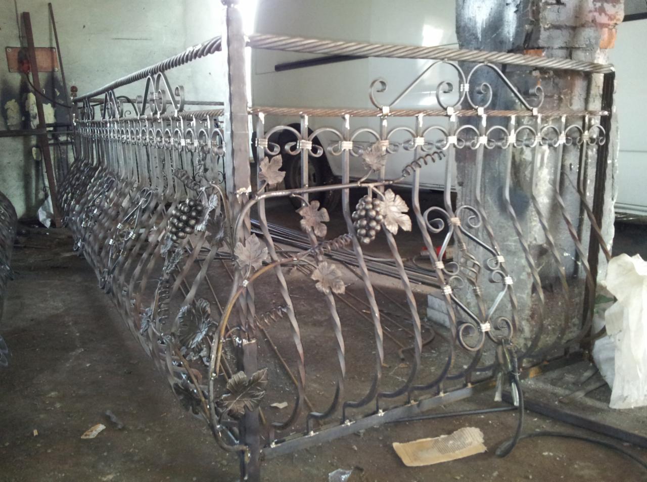 Kuty balkon z motywem winogron, surowy metal, warsztat. Dekoracyjne elementy i spiralne zdobienia. Widok z boku, nieostre tło.