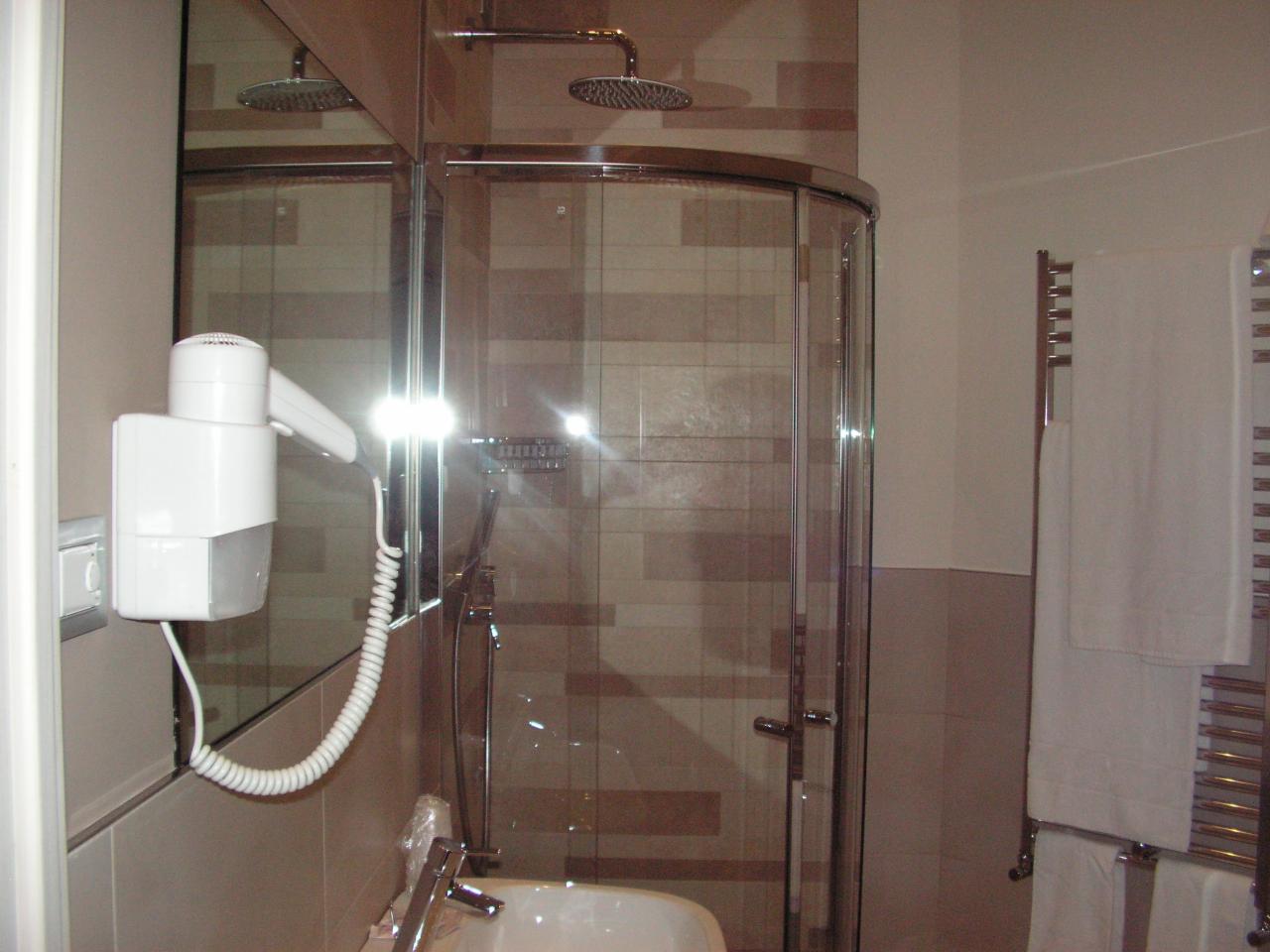 Umeblowana łazienka z kabiną prysznicową z zaokrąglonym szkłem, białą suszarką do włosów zamontowaną na ścianie, grzejnikiem drabinkowym z wiszącymi ręcznikami i lustrem.