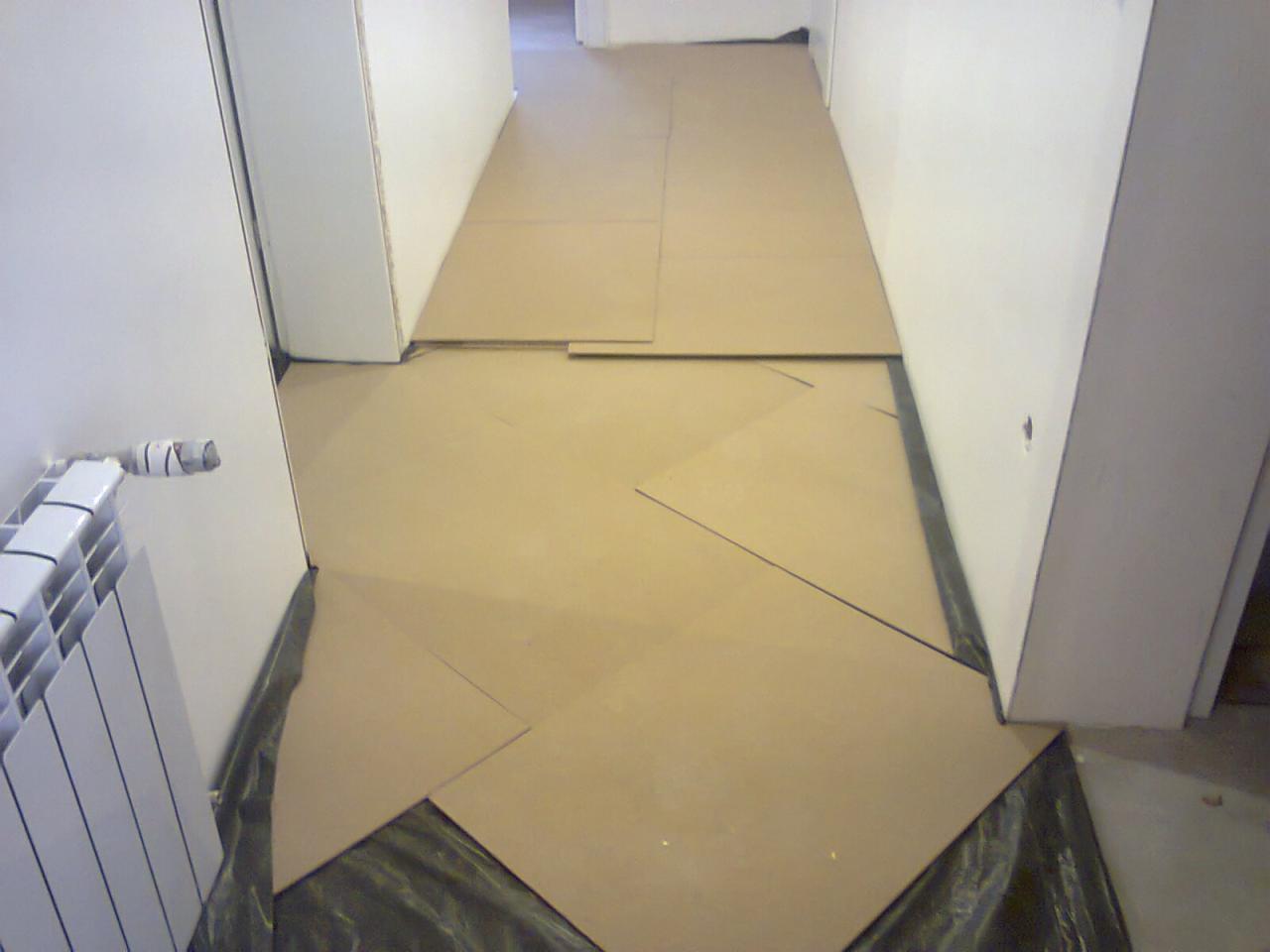 Korytarz w trakcie zabezpieczania podłogi kartonem i folią malarską przed remontem. Grzejnik żeberkowy przy ścianie po lewej.