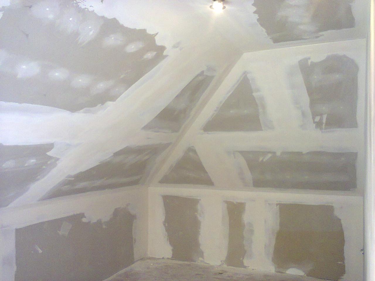 Sufit poddasza z widoczną konstrukcją szkieletową i nałożoną warstwą gładzi gipsowej, przygotowany do dalszych prac wykończeniowych, oświetlony przez pojedynczą lampę sufitową.