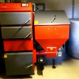 Kotłownia z automatycznym podajnikiem paliwa stałego marki Tekla, obok zasobnik ciepłej wody użytkowej, widoczne rury instalacyjne i elementy kotła