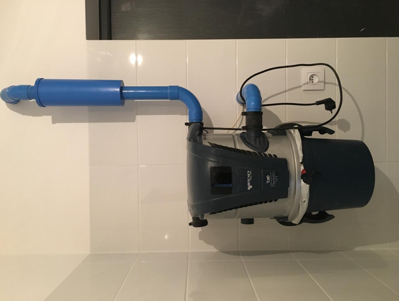 Szara pompa hydroforowa marki Italtecnica TUBO Perfetto 100L z niebieskimi rurami podłączona do instalacji w pomieszczeniu z białymi płytkami.