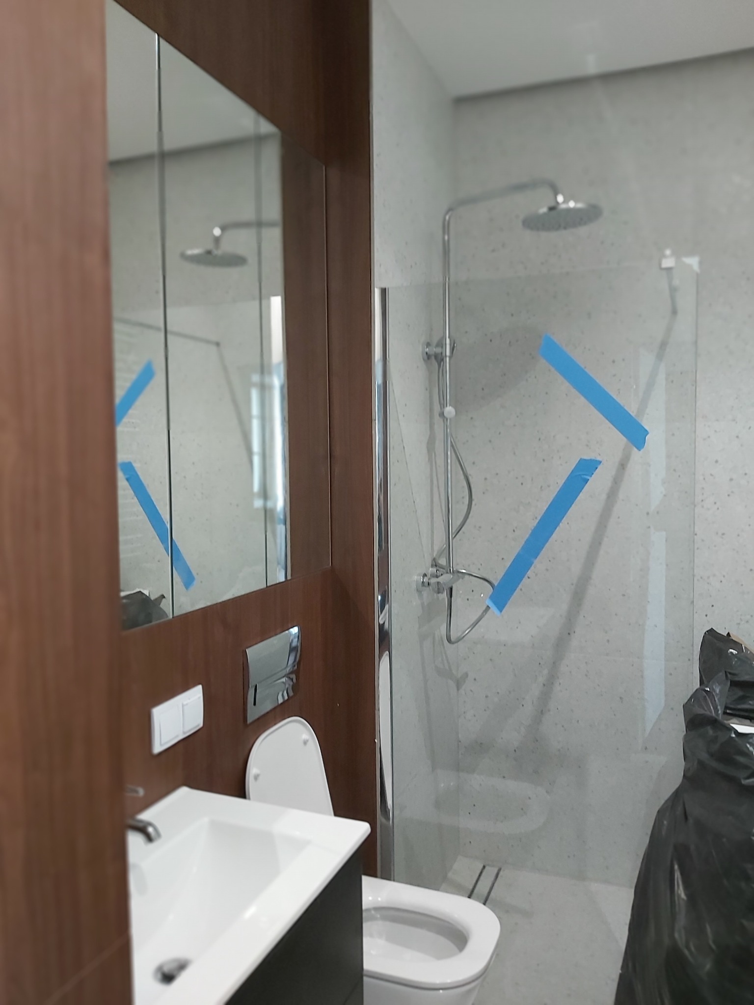 Nowoczesna łazienka w trakcie wykańczania: biała umywalka z szafką, toaleta, szklana kabina prysznicowa z taśmą zabezpieczającą i armaturą.