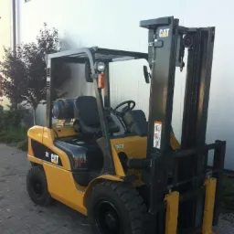 Żółty wózek widłowy marki CAT, model 35, sfotografowany z boku na tle białej hali i zieleni.