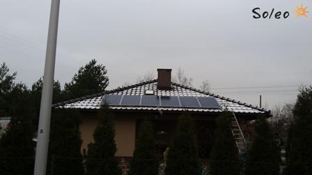Panele słoneczne zamontowane na dachu domu jednorodzinnego, częściowo pokrytym śniegiem, drabina oparta o dach, widoczne logo firmy Soleo w prawym górnym rogu.