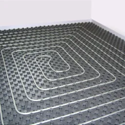 Układ ogrzewania podłogowego z rurkami ułożonymi w spiralny wzór na czarnej izolacji, widok z góry na fragment podłogi przy ścianie.