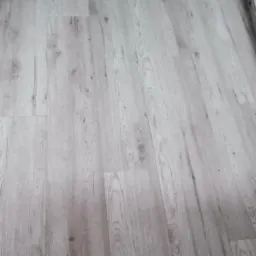 Ułożona podłoga z paneli imitujących jasne drewno z widocznym wzorem słojów, ułożonych równolegle do siebie.