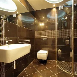 Nowoczesna łazienka z ciemnymi płytkami i mozaiką, kabiną prysznicową ze szklanymi drzwiami, podwieszaną umywalką i toaletą.