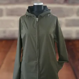 Khaki, wodoodporny płaszcz z kapturem zapinany na zamek, eksponowany na manekinie na tle ceglanej ściany.