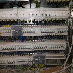 Otwarta skrzynka elektryczna z licznymi przewodami, bezpiecznikami i modułami Legrand oraz Schneider Electric, widoczne oznaczenia ROL1, ROL2, WYB2, F1.1, F2.1, FP1, FP2, FP3, FP4, FP5, F3.1, F4.1,...