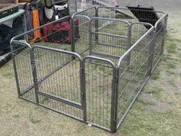 Metalowy kojec z siatki, z zaokrąglonymi narożnikami, ustawiony na trawie, widoczne torby i wózki w tle.