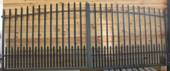 Metalowa brama dwuskrzydłowa z ostrymi zakończeniami prętów, wykonana w Kielcach, na tle drewnianej ściany.